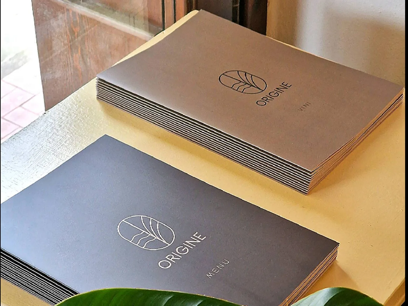 Le brochure del menu di Origine Ristorante con il logo dorato e una foglia